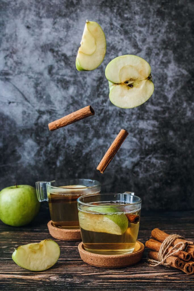 Apples slices falling into two glass teacups with hot tea and cinnamon sticks.